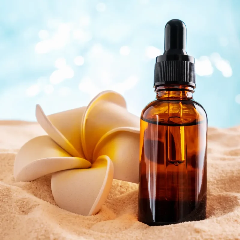brown-glass-bottle-with-plumeria-flower-on-a-sandy-2025-03-06-02-43-46-utc